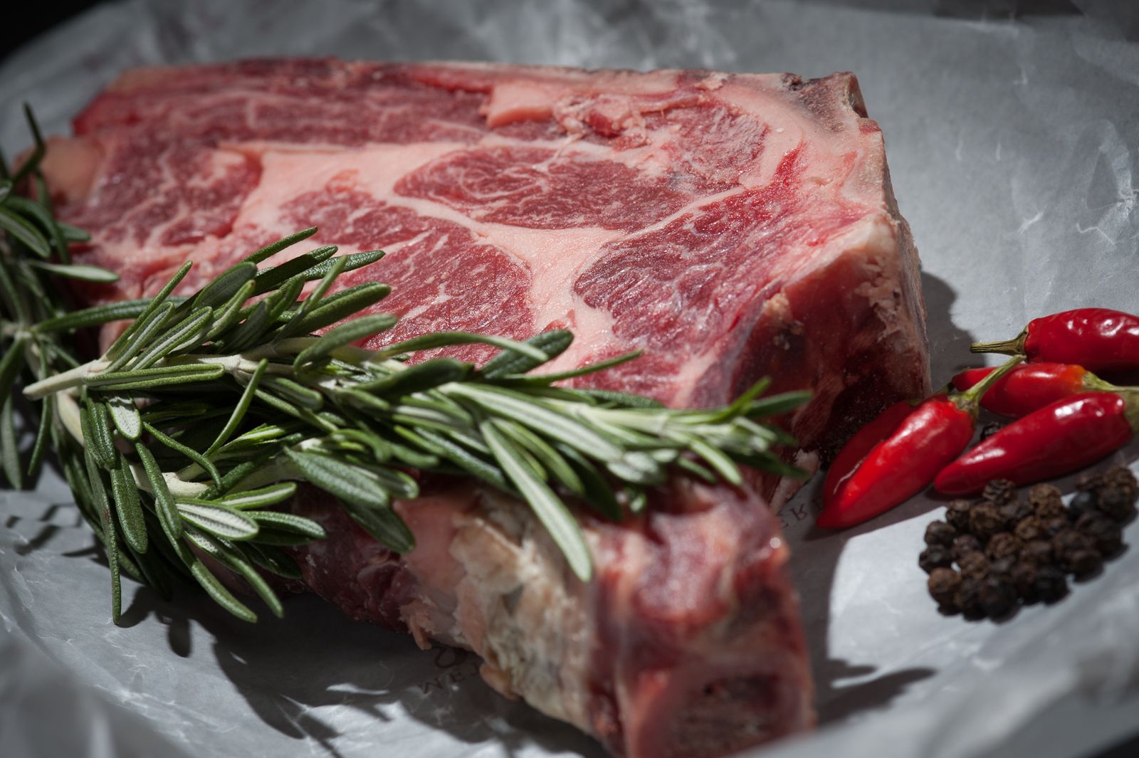 Côte de bœuf crue au romarin sur fond noir, avant la braise