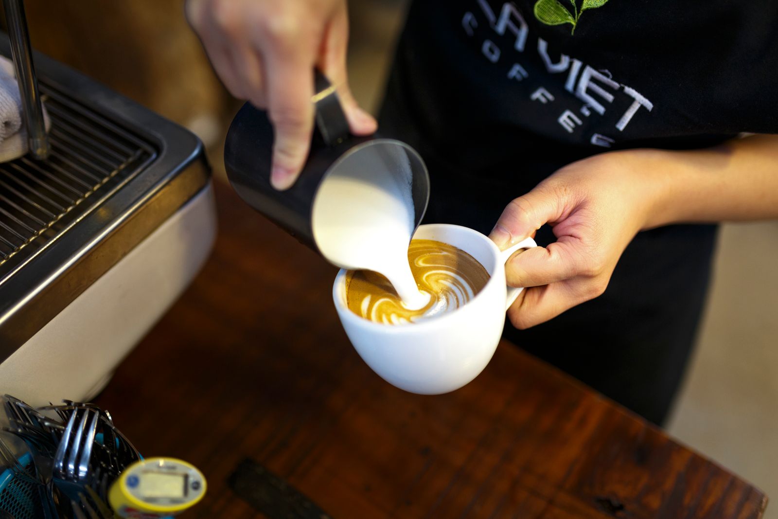 Les mains du torréfacteur versant le lait sur un café, au comptoir