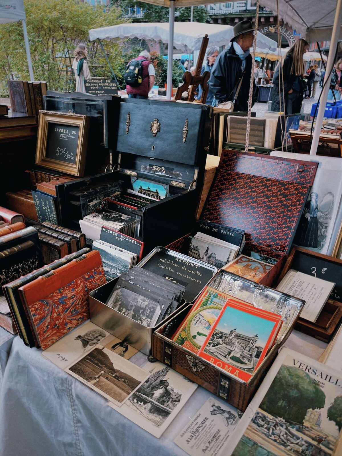 Les livres anciens et les boîtes de cartes postales d'un étal de bouquiniste, prix à l'ardoise