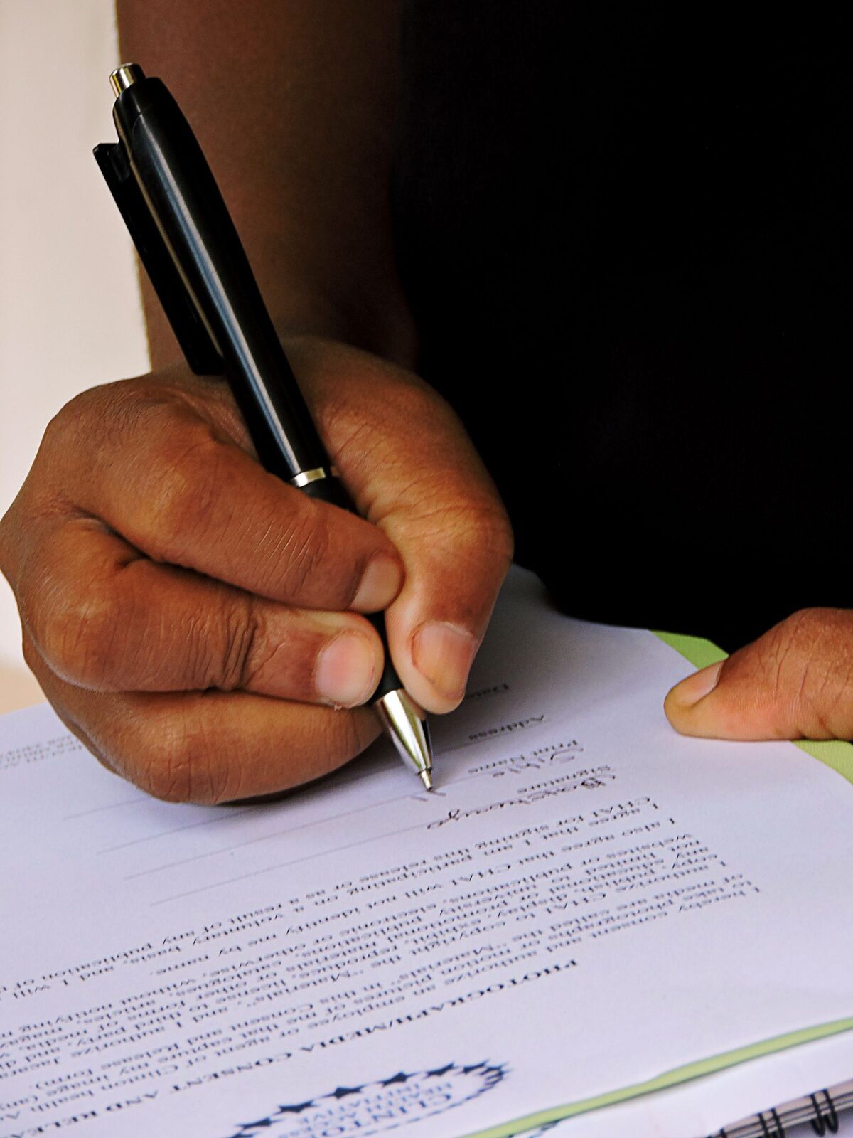 Une main remplit au stylo le formulaire d'une pré-demande, au guichet