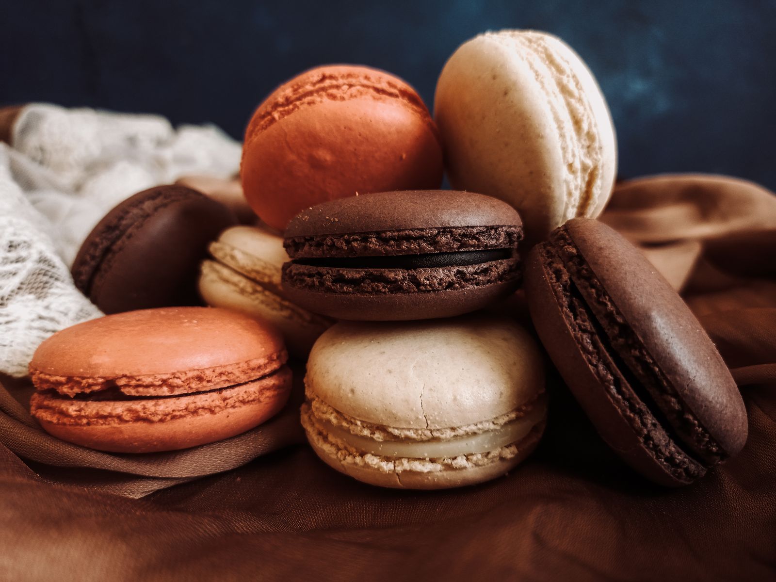 Macarons caramel, chocolat et vanille posés sur un drapé cuivré