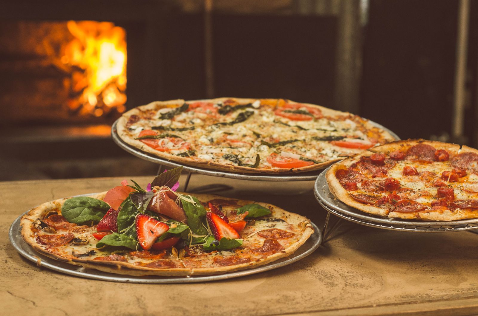 Trois pizzas devant la gueule du four à bois