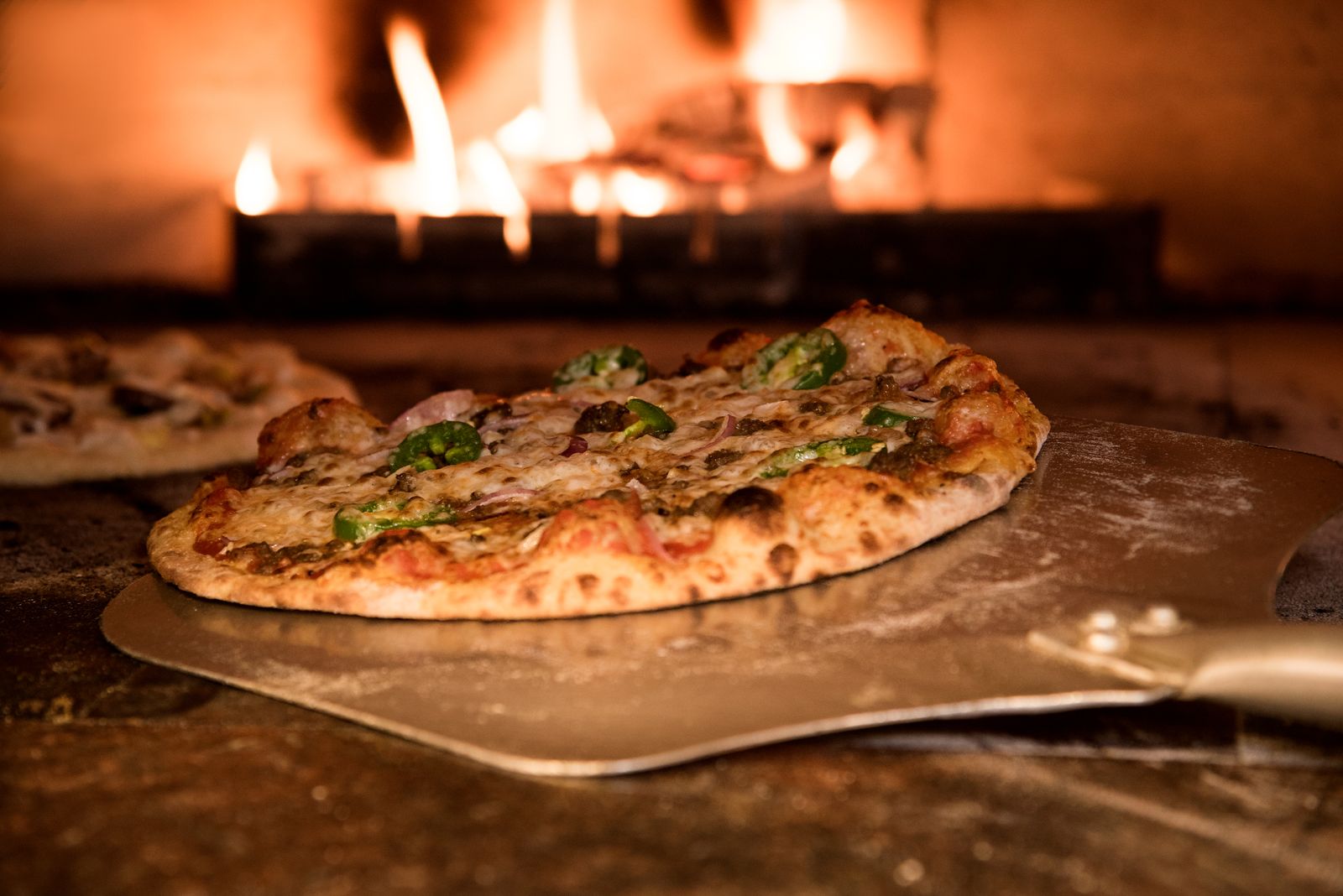 Pizza sur pelle devant les flammes du four à bois