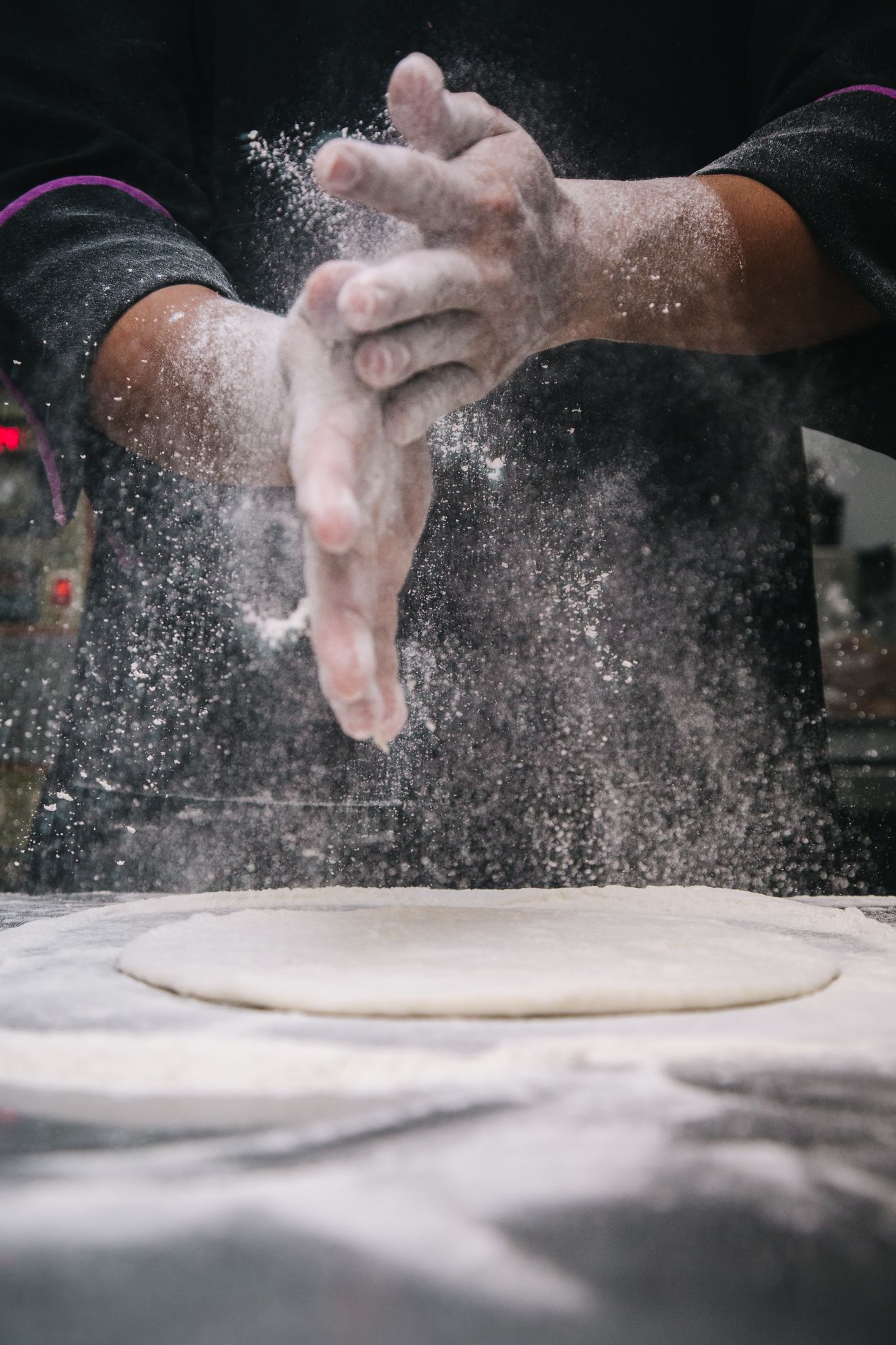Les mains du pizzaïolo dans un nuage de farine au-dessus de la pâte étirée